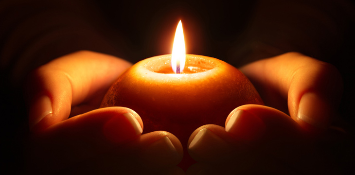 A round lighted candle held in the palm of a person's hands